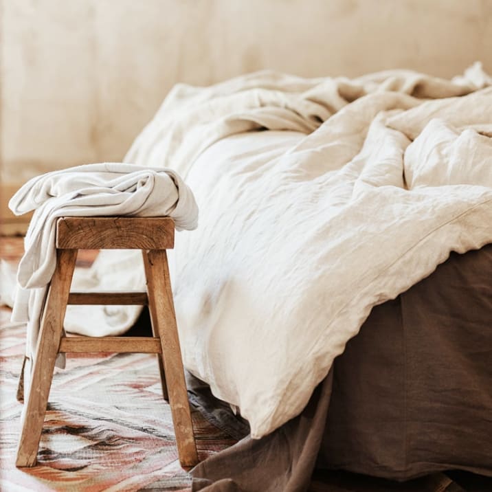 White bed linen on a bed and piled on a stool in a bedroom